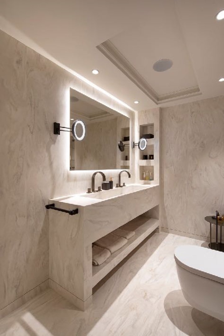 Floor and walls cladding, vanity unit with seamlessly integrated washbasin, towel rack and niches in Corian<sup>®</sup> Carrara Crema colour (left). Behind the bathtub, wall cladded in Smoke Drift Prima Corian<sup>®</sup>, complemented by concealed lighting. Design by Soliform; pictures © Dian Stanchev, all right reserved.